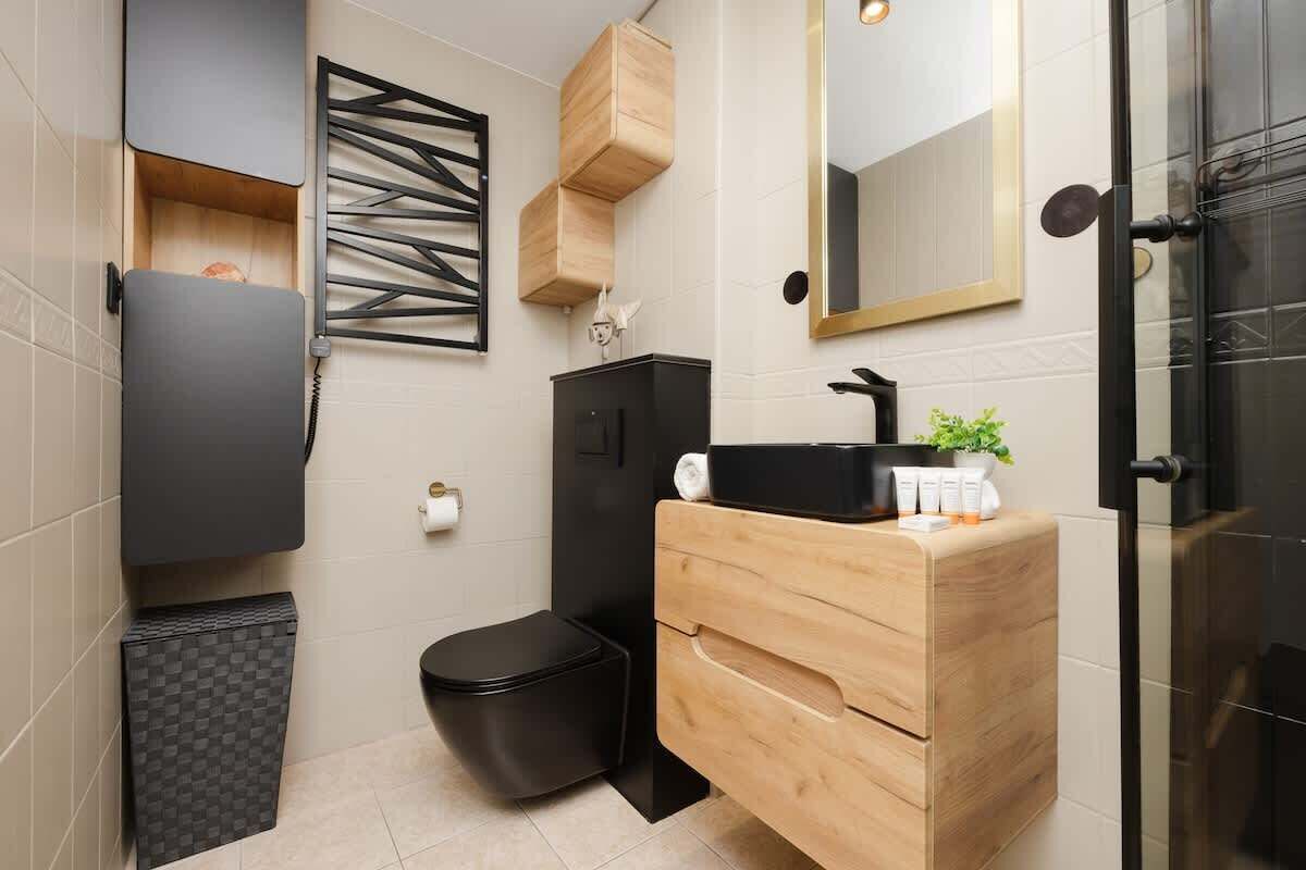 Ein modernes Badezimmer mit Toilette in Schwarz, einem Holzbadezimmermöbel mit Spiegel und einem Waschbecken in Schwarz.