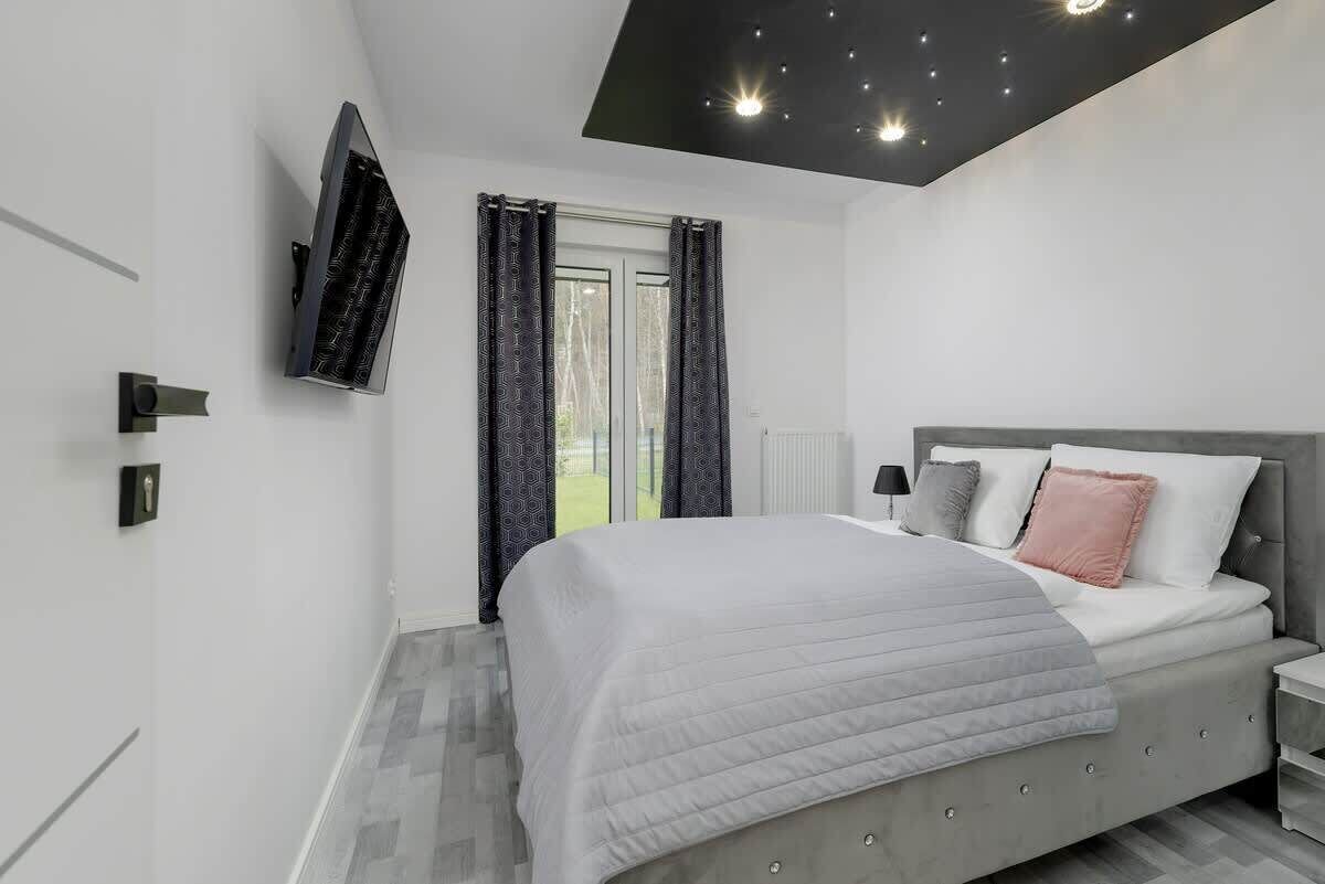 A modern bedroom with a bed, a TV mounted on the wall, and a window with curtains.