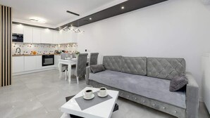 Una cocina moderna con armarios blancos, una mesa de comedor con sillas y un sofá gris en la sala de estar.