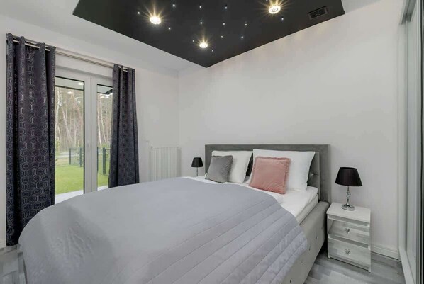 A modern bedroom with a large bed, a nightstand, and a window with curtains.