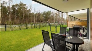 Un balcón con mesa y sillas, vista a un área verde y una valla de madera.