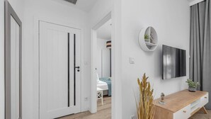 Un interior modern amb una porta blanca, una taula consola de fusta, un televisor penjat i una planta.