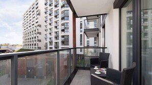 En balkon med gelænder af glas, en sort fletsofa og et bord med et par ting på.