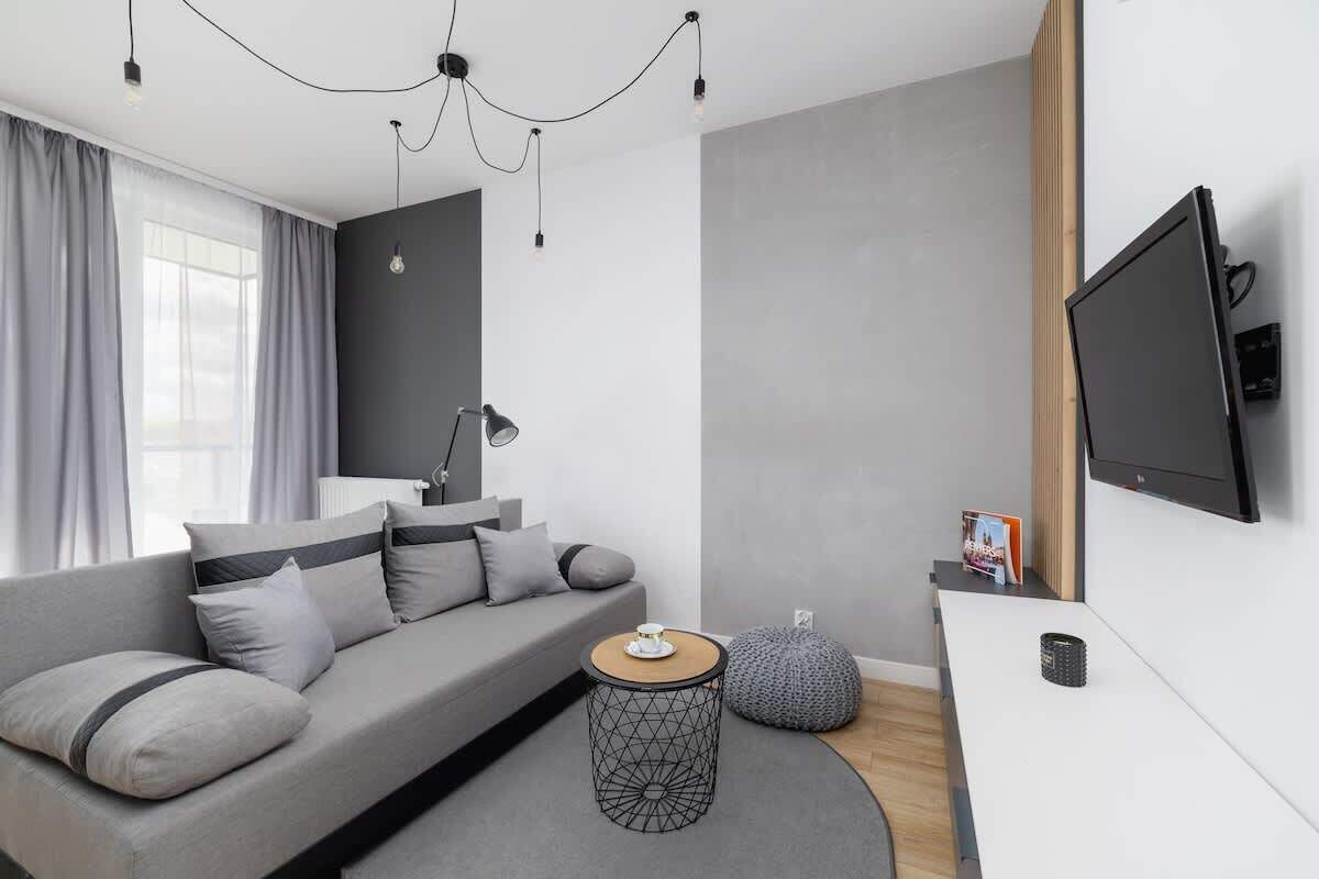 Un salon moderne avec un canapé gris, une table basse ronde et un téléviseur à écran plat fixé au mur.