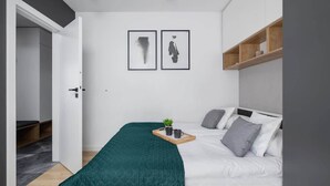Et moderne soveværelse med en seng, et natbord med bakke, en lille plante og to billeder i rammer på væggen.