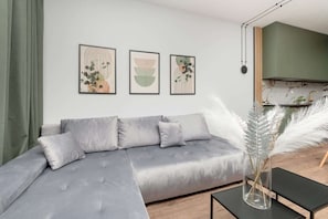 Un salón moderno con un sofá seccional gris, un jarrón de vidrio con plumas de pampa y arte abstracto en la pared.