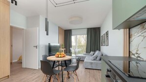 Ein modernes Wohnzimmer mit Essbereich, einem grauen Sofa, einem Fernseher und einer Küchenzeile mit Marmorrückwand.
