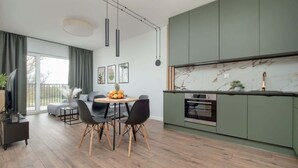 Eine moderne Küche mit grünen Schränken, einer Marmor-Spritzschutzwand und einem Essbereich mit rundem Tisch und Stühlen.