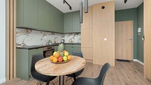 Eine moderne Küche mit grünen Schränken, einer Marmor-Spritzschutzleiste und einem Essbereich mit einem runden Holztisch und schwarzen Stühlen.