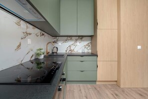 Una cocina moderna con encimera negra, armarios verdes y salpicadero de mármol.