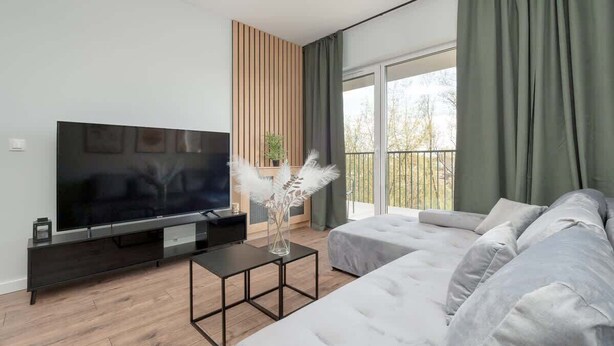Ein modernes Wohnzimmer mit Flachbildfernseher, einer Couch, einem Couchtisch und Blick ins Freie.