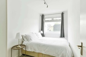 Een slaapkamer met een bed, nachtkastje, lamp en een raam met gordijnen.