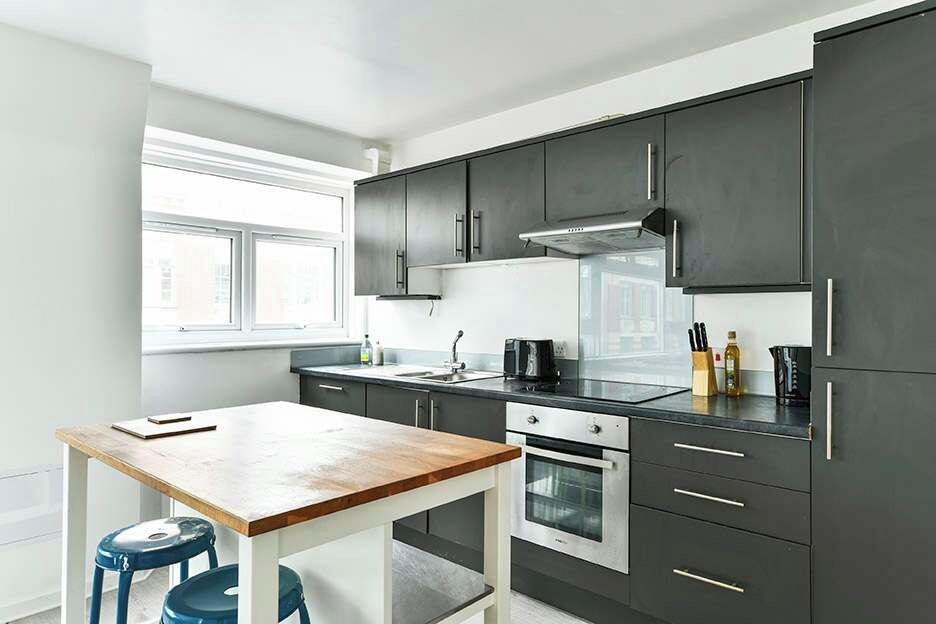 A modern kitchen with dark cabinets, a wooden table, and two blue stools.