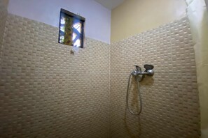 Une douche avec un mur beige à texture, une petite fenêtre et un pommeau de douche.