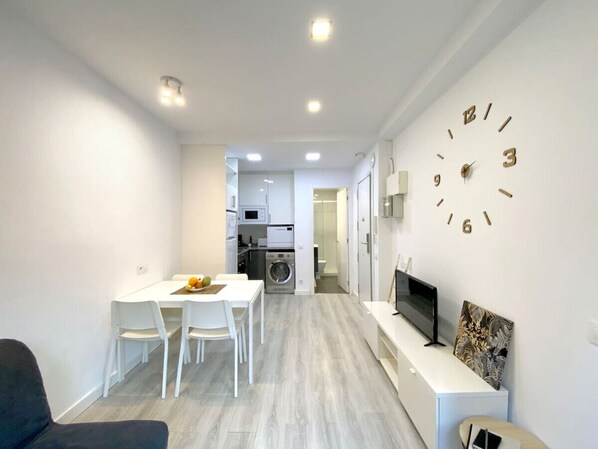 A modern, compact living space with a dining area, kitchenette, and a large wall clock.