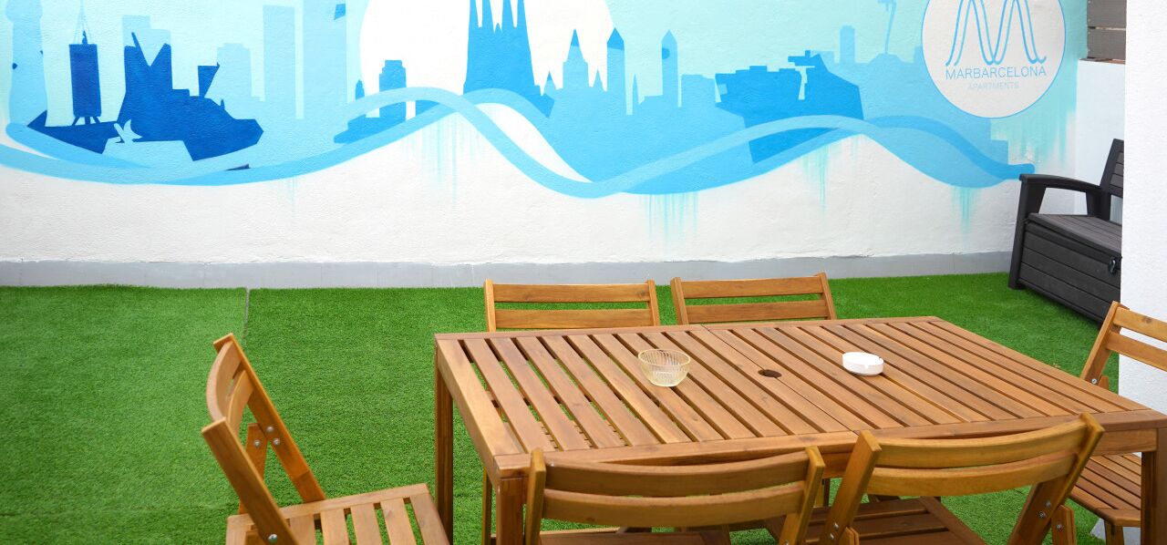 Zona pranzo con tavolo e sedie in legno, pavimento in erba sintetica verde e un murale con skyline di una città sulla parete.