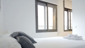 A hotel room with a bed, pillows, a window, and a fruit bowl.