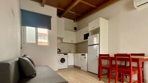 Un espacio habitable compacto con sofá, una mesa de comedor con sillas, lavadora y refrigerador.