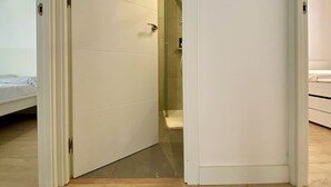 Una habitación de hotel con una cama, un armario blanco y una cabina de ducha de cristal.