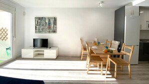 A modern living room with a dining area, a flat-screen TV, and a cityscape painting on the wall.