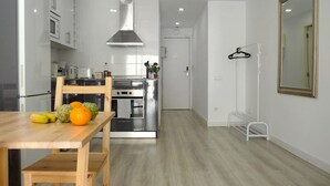 A modern kitchen with white cabinets, a stainless steel range, and a wooden dining table with fruits.