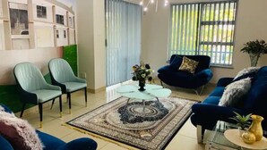Un salon avec un canapé bleu, deux fauteuils bleu clair, une table basse en verre et un tapis à motifs.