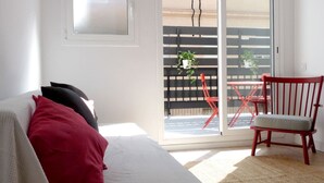 A room with a sofa, a red chair, and a sliding glass door leading to an outdoor area with a red chair and a plant.