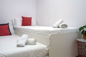 Ein Hotelzimmer mit drei Betten, jedes mit weißer Bettwäsche und roten Kissen. Ein kleiner runder Tisch mit einer Pflanze darauf.