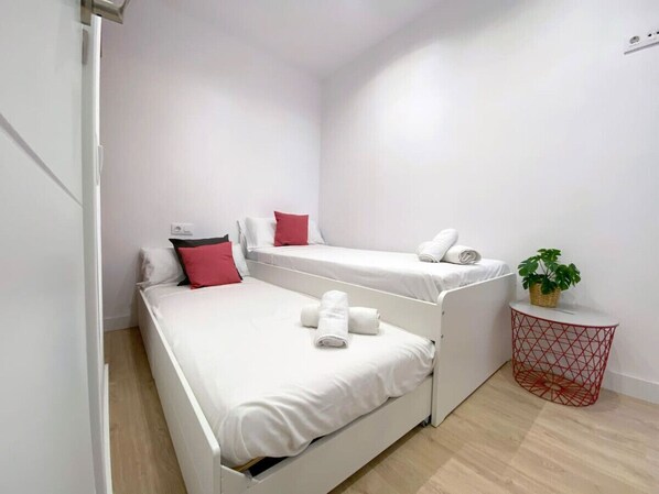 Un dormitorio con dos camas, una mesita con una planta y una cesta roja.