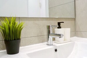 Ein Badezimmer mit einem weißen Waschbecken, einem chromfarbenen Wasserhahn und einem schwarzen Seifenspender.