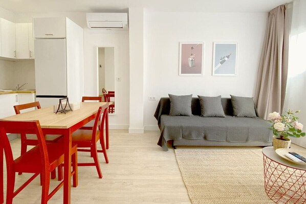 Ein modernes Wohnzimmer mit einer Couch, einem Esstisch mit Stühlen und einem sichtbaren Küchenbereich durch eine offene Tür.