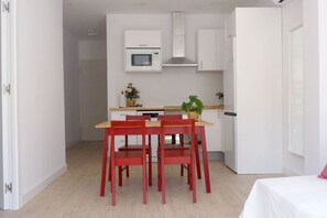 A compact kitchen with white cabinets, a microwave, and a stove. There is a dining table with four red chairs and a potted plant on it.