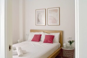 A neatly made bed with white and pink pillows, a wooden headboard, and two framed artworks on the wall.