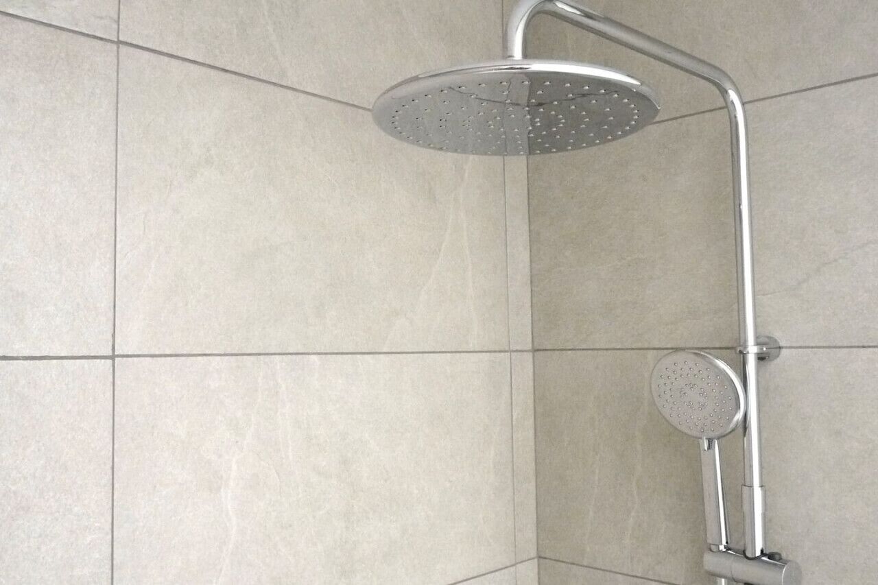 Ducha con cabezal de ducha de mano y cabezal de ducha fijo en el techo, en un baño con azulejos.