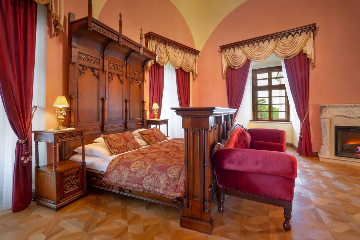 Un dormitorio tradicional con cama con dosel, un sillón rojo y una chimenea.