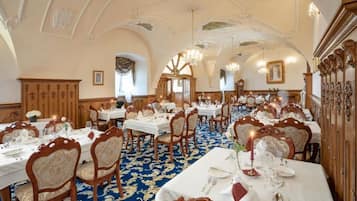 Un salón comedor imponente con candelabros ornamentales, paneles de madera y suelo cubierto de alfombra azul.