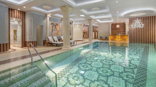 A luxurious indoor swimming pool with a patterned floor, a reception area, and seating by the pool. - Galicia Nueva castle hotel (Halic)