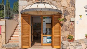 A stone building with a wooden door and shutters, a staircase to the left, and a potted plant on the right. - Holiday apartment with swimming pool and air conditioning (Budoni)