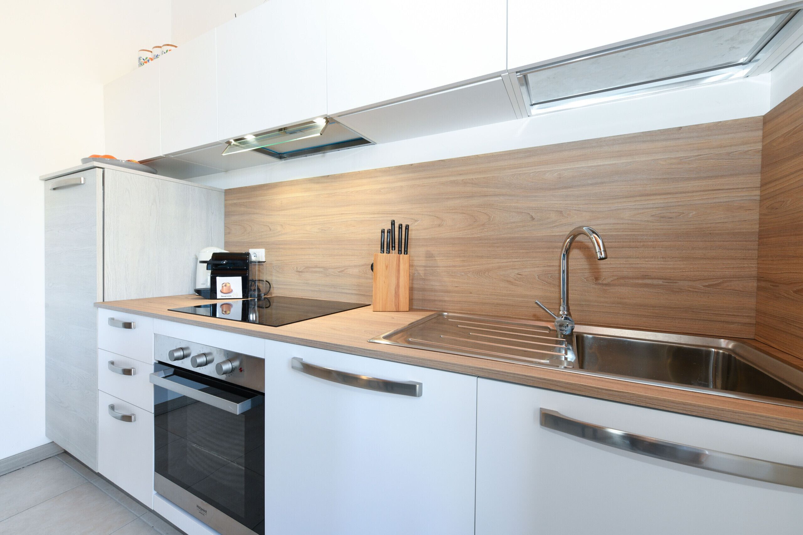 A modern kitchen with white cabinets, a wooden backsplash, stainless steel appliances, and a knife block.