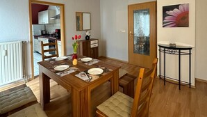 A dining area with a wooden table set for four, chairs with cushioned seats, a small side table, and a ceiling light fixture.