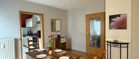 Comedor con mesa de madera dispuesta para cuatro, sillas con asientos acolchados, una mesita auxiliar y una lámpara en el techo.