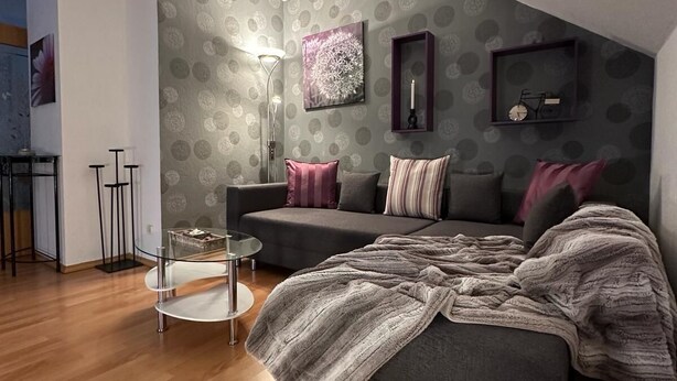 A modern bedroom with a grey sofa, a round coffee table, and a large bed with a grey blanket.