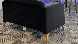 Un salon moderne avec un canapé noir, un bureau et une chaise. Un grand tableau orne le mur et une fenêtre laisse entrer la lumière naturelle.