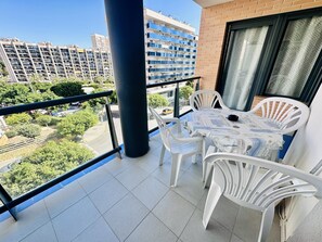 A balcony with white plastic chairs and a table, a large black pillar, and a view of a cityscape with buildings and trees. - A1047 - Nice apartment in a complete urbanisation and close to the beach (Villajoyosa)