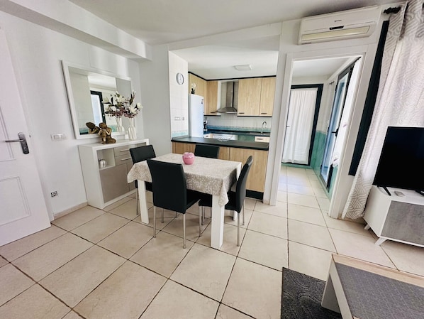 Cocina compacta con comedor, televisor y un amplio ventanal.