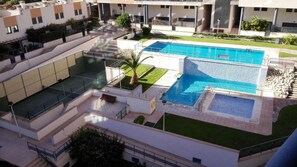 Una piscina en la azotea con una pequeña cascada, rodeada de un césped cuidado y un edificio de varios niveles con balcones.