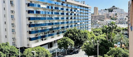 Un hotel de varios pisos con balcones, un estacionamiento y vistas a un paisaje urbano montañoso.