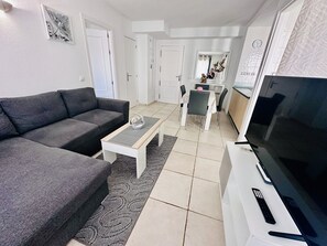 Una sala de estar con un sofá gris, una mesa de centro, un televisor y un comedor con sillas y una mesa.