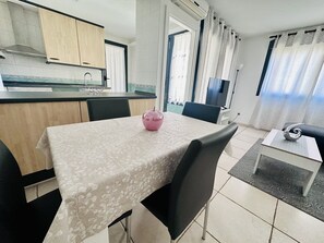 Una cocina moderna con armarios de madera, una mesa de comedor con un centro de mesa rosa y una sala de estar con un sofá y televisión.
