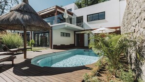 Une maison moderne dotée d’une piscine, d’une terrasse en bois et d’un parasol en chaume.